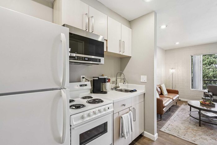 Cozy and modern kitchen with sleek appliances leading into a bright and inviting living area featuring elegant furniture and large windows.