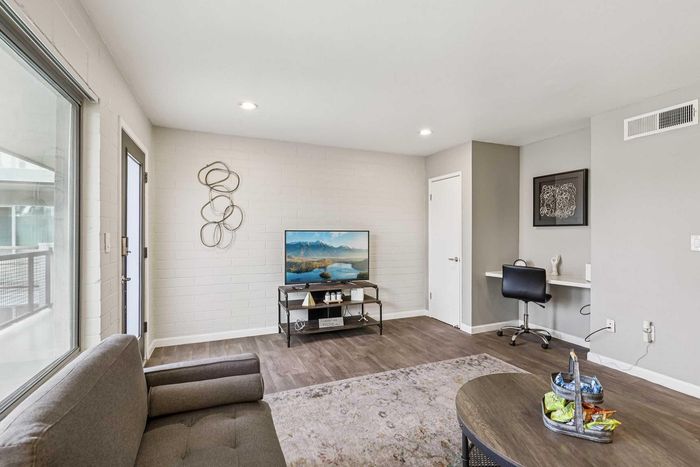 Modern living room with stylish decor, featuring a cozy sofa, elegant wall art, and a flat-screen TV on dark hardwood floors.