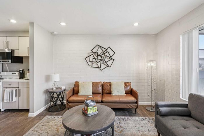 Charming living room with modern decor, featuring a stylish leather sofa, cozy armchair, and sleek open kitchen design.