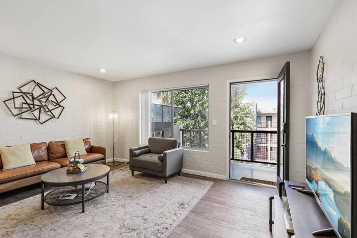 Bright and modern living room with stylish decor, a cozy leather couch, and a wall-mounted TV, opening to a scenic balcony view.