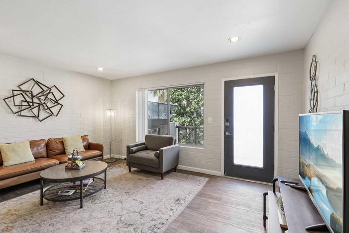 Inviting living room with modern decor, cozy brown leather sofa, large window for natural light, and stylish wall art, ideal for relaxation and entertainment.