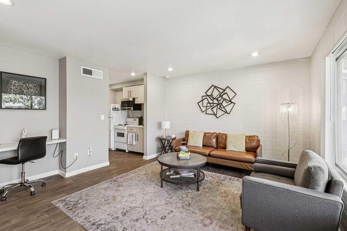 Chic modern living room with a cozy leather sofa, abstract wall art, and open-concept layout leading to a stylish kitchen.