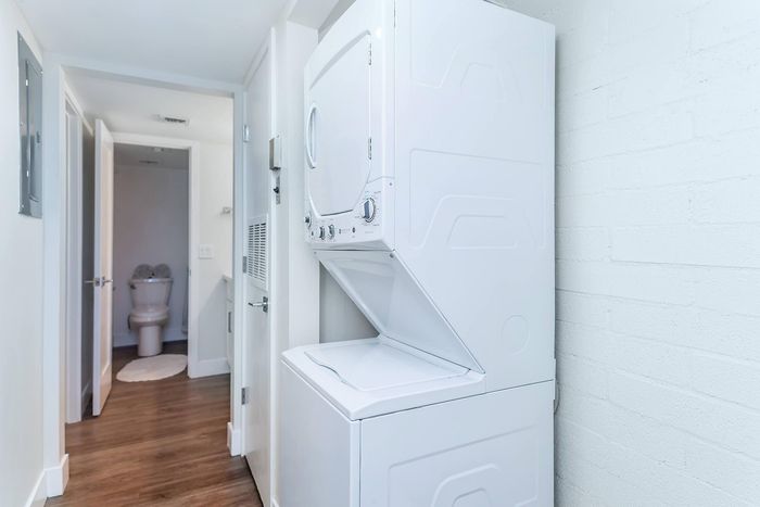 Convenient in-unit stacked laundry set within a bright, modern apartment hallway leading to a chic bathroom.