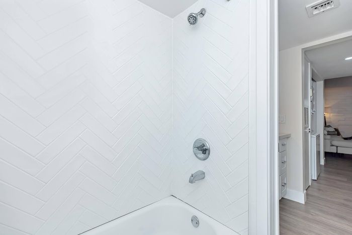 Elegant bathroom with modern herringbone tile design, featuring updated shower fixtures and sleek cabinetry in a stylish apartment setting.