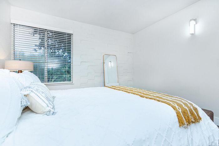 Bright, cozy bedroom with a white brick accent wall, large window, and mirror reflecting natural light.