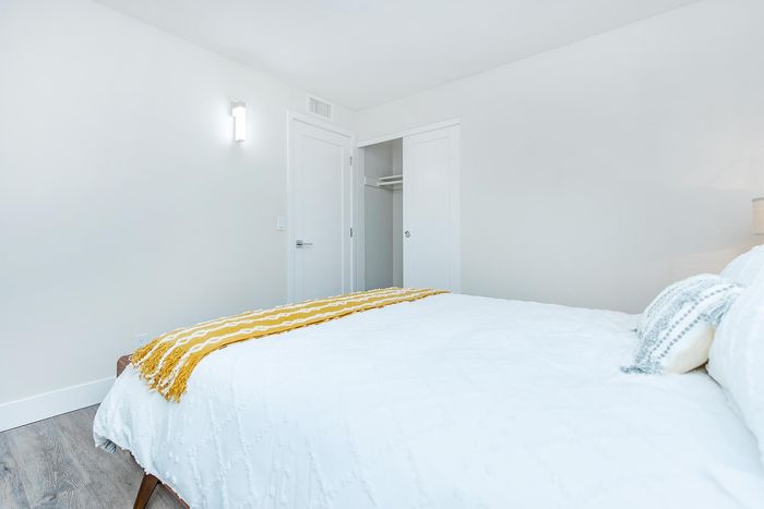 Bright and inviting bedroom with modern closet, featuring a cozy bed adorned with a yellow throw and stylish pillow accents.