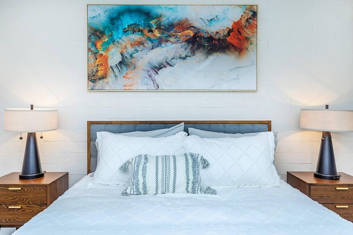 Elegant bedroom featuring crisp white bedding, textured pillows, and contemporary bedside lamps, enhanced by vibrant abstract wall art.
