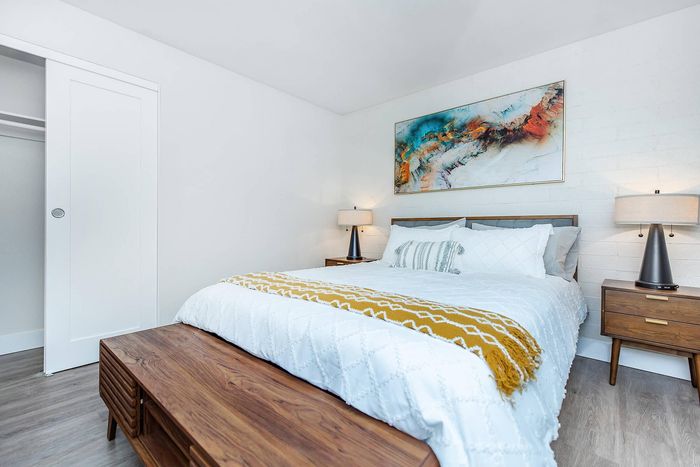Elegant bedroom with a modern wooden bed, stylish white bedding, and vibrant abstract art. Cozy ambiance highlighted by sleek bedside lamps and a minimalist design.