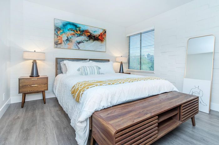 Bright and modern bedroom featuring elegant decor, a plush bed with white linens, and stylish wooden furniture.