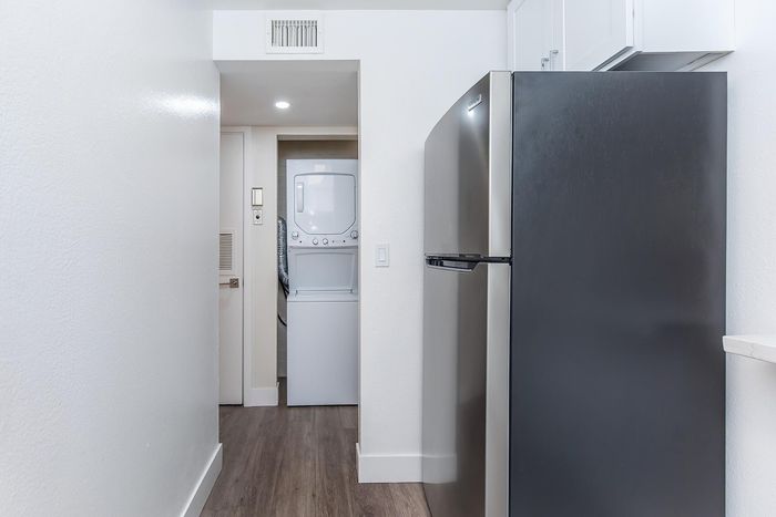 Modern apartment kitchen hallway showcasing a sleek stainless steel refrigerator and in-unit stacked washer and dryer, enhanced by elegant wood flooring.