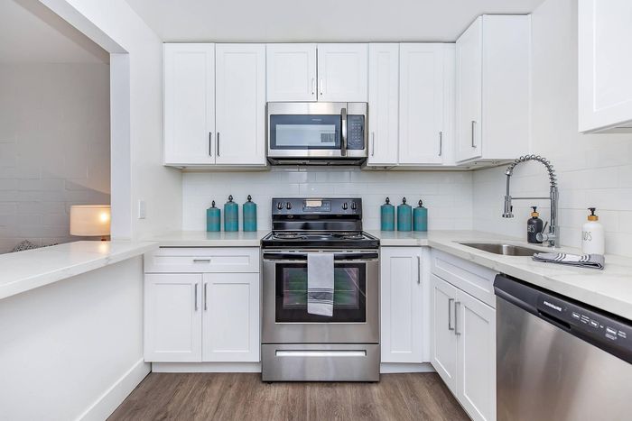 Sleek modern kitchen with stainless steel appliances, white cabinetry, and elegant countertop with warm wood flooring.