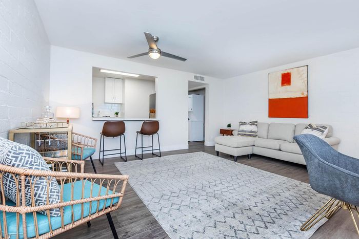 Bright and modern living room featuring stylish rattan chairs, a plush beige sectional sofa, and an elegant open-concept kitchen with sleek bar seating.