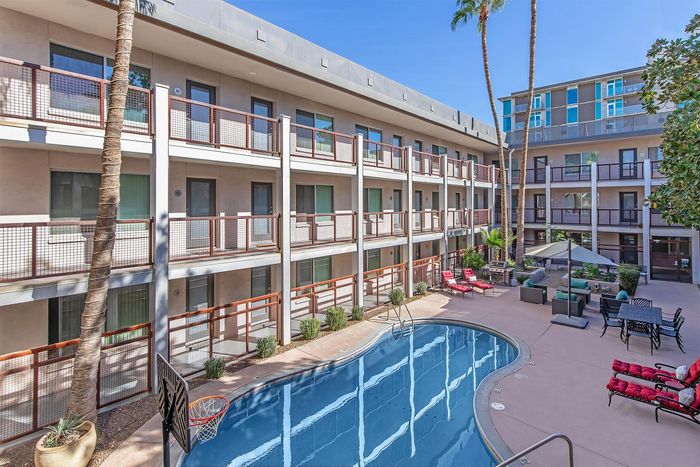 Chic apartment complex with a sunlit courtyard, featuring a crystal clear pool, relaxing lounge chairs, and lush greenery.