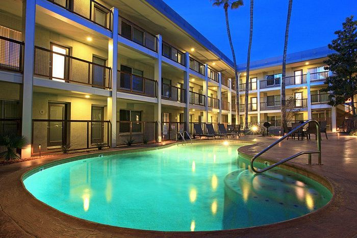 Elegant courtyard at dusk showcasing a luminous pool surrounded by modern three-story apartments and tall palm trees.
