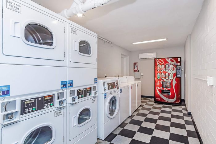 Modern and bright laundry room equipped with ample washers, dryers, and a convenient soda vending machine, set against stylish checkered flooring.