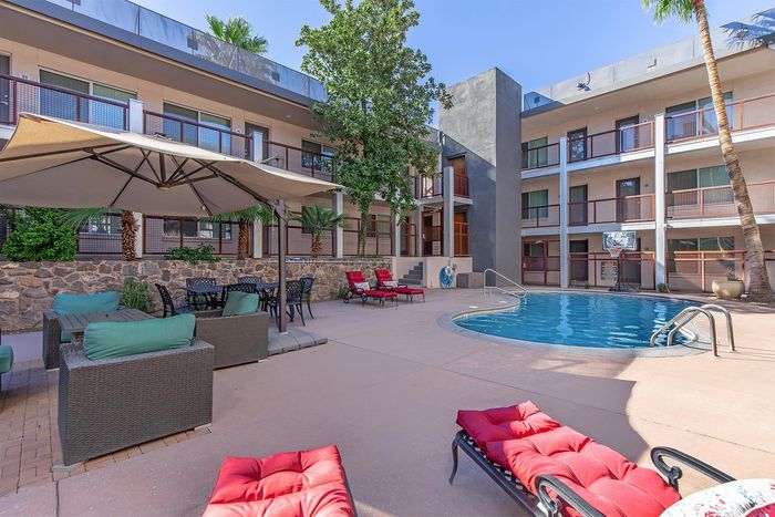 Luxurious apartment courtyard featuring a sparkling pool, chic lounge chairs, and shaded seating areas surrounded by lush greenery.