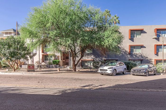 Charming apartment exterior with modern windows, lush trees, and convenient parking, perfect for comfortable urban living.