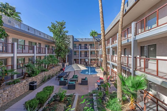 Charming apartment complex courtyard featuring lush palm trees, a sparkling pool, and cozy outdoor seating area under clear blue skies.