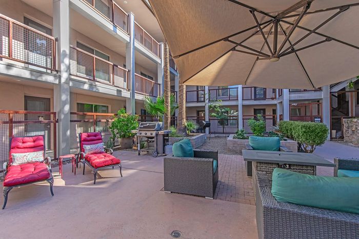 Inviting outdoor patio featuring cozy seating, vibrant landscaping, and a modern barbecue grill under a spacious umbrella in a stylish apartment complex.