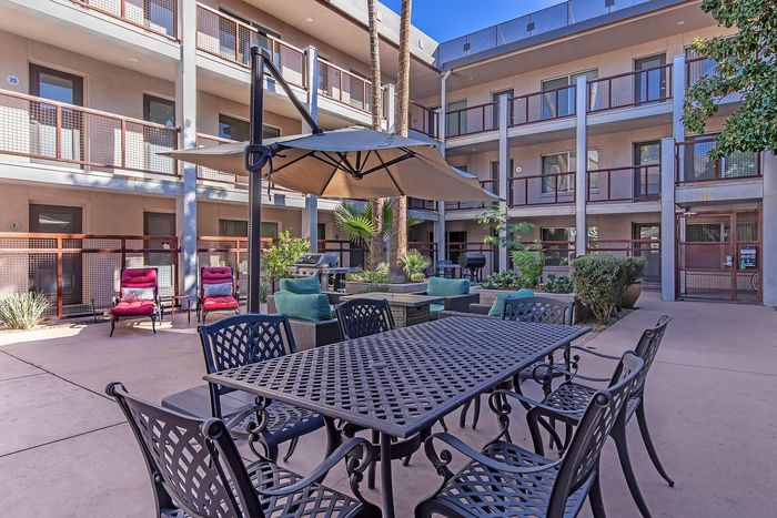 Charming apartment courtyard featuring lush greenery, outdoor seating, and BBQ grill, perfect for relaxation and entertaining.