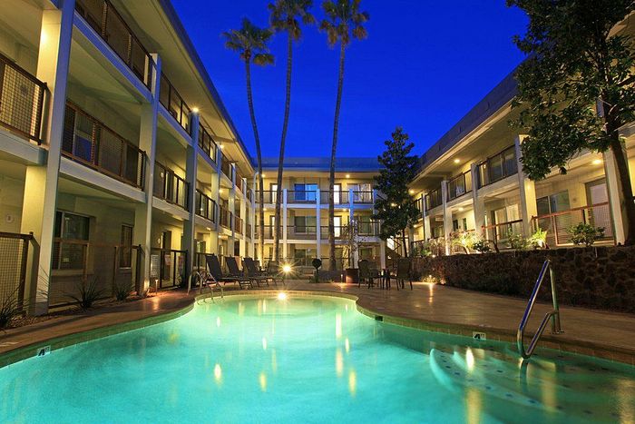 Elegant apartment complex at dusk featuring a serene swimming pool and inviting patio area surrounded by lush greenery and modern balconies.