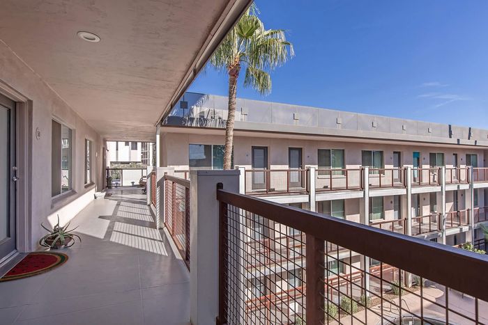 Chic apartment balcony with modern railing, vibrant palm tree, and sunlit views in a stylish residential complex.