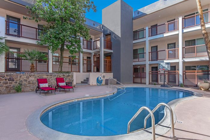 Inviting apartment complex courtyard with serene pool, lush trees, and comfortable lounge chairs.