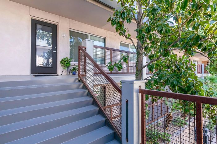 Charming apartment entrance with modern steps, lush greenery, and a stylish metal railing.