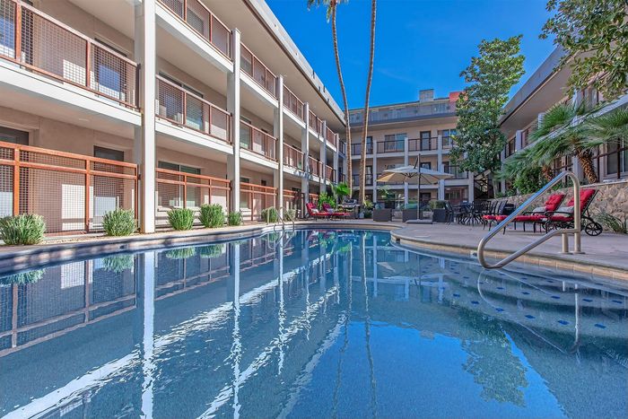 Luxurious apartment complex featuring a sparkling outdoor pool with stylish lounge areas, surrounded by lush greenery and contemporary architecture.