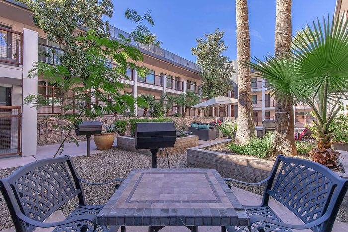 Charming outdoor patio in a modern apartment complex, featuring lush greenery, stylish seating, and barbecue grills for relaxation and entertainment.