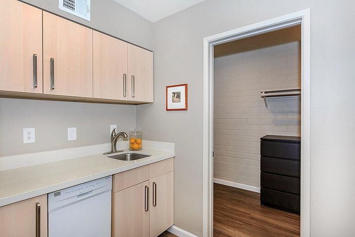 Elegant kitchen area with pristine countertops, modern sink, and ample storage cabinets, adjacent to a spacious pantry with shelving.