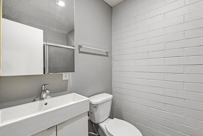 Modern bathroom with sleek white fixtures, a chic wall-mounted sink, and stylish gray brick accent wall.