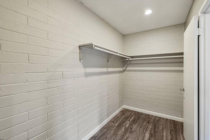 Spacious walk-in closet with modern shelving and wood-style flooring, ideal for ample storage and organization.