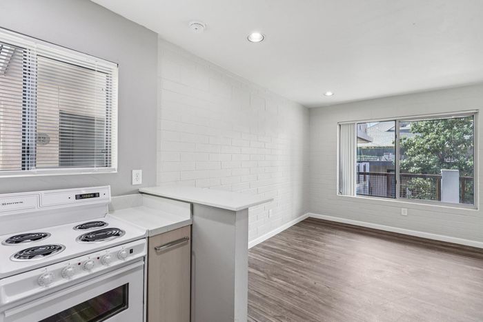 Bright, modern open-plan living area with sleek hardwood floors, cozy kitchen, and large windows offering natural light and outdoor views.