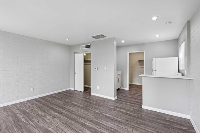 Modern apartment interior featuring elegant wood flooring, a sleek kitchen with white appliances, and spacious closet space for streamlined living.
