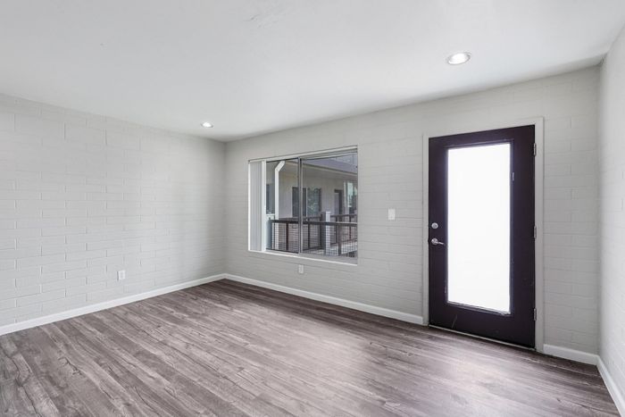 Modern apartment interior with sleek wood flooring, large window, and bright glass door enhancing natural light.
