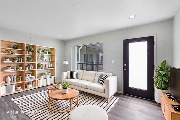 Bright and inviting living room with a cozy white sofa, stylish striped rug, abundant greenery, and modern shelving, creating a welcoming and tranquil atmosphere.