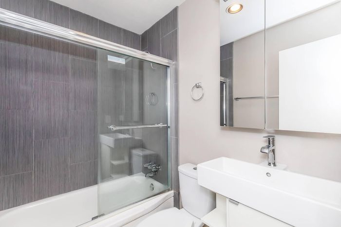 Modern bathroom featuring sleek gray tiles, a glass-enclosed bathtub, and a spacious white vanity with a mirror cabinet.