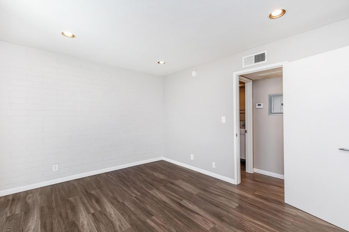 Bright and airy room with sleek wood flooring, modern recessed lighting, and a fresh white brick accent wall.