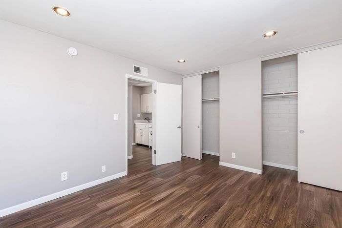 Bright and airy room showcasing modern wood flooring, sleek closets, and open access to the contemporary kitchen.