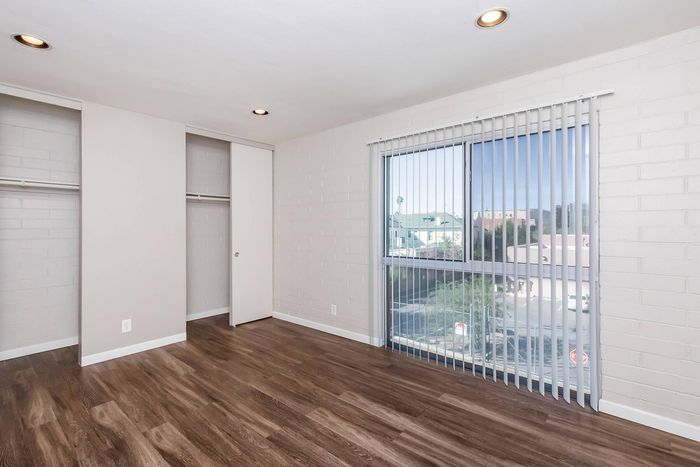 Bright and airy bedroom with elegant wooden flooring, large closet space, and a sunlit window providing urban views.