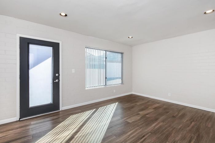 Bright, modern apartment room with sleek wooden floors, stylish black framed door, and ample natural light.