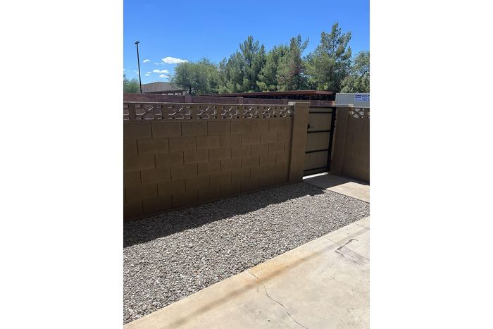 Charming outdoor space with a secure gate, gravel courtyard, and scenic view of lush trees under a bright blue sky.