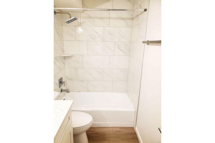 Elegant modern bathroom featuring a sleek bathtub with overhead shower, polished tile walls, and chic wooden flooring.