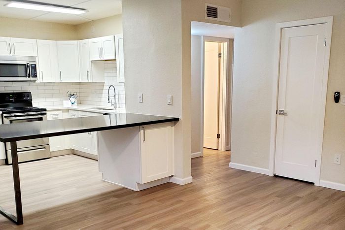 Modern kitchen space with sleek black countertops, white cabinetry, and stainless steel appliances, seamlessly connecting to an inviting living area.