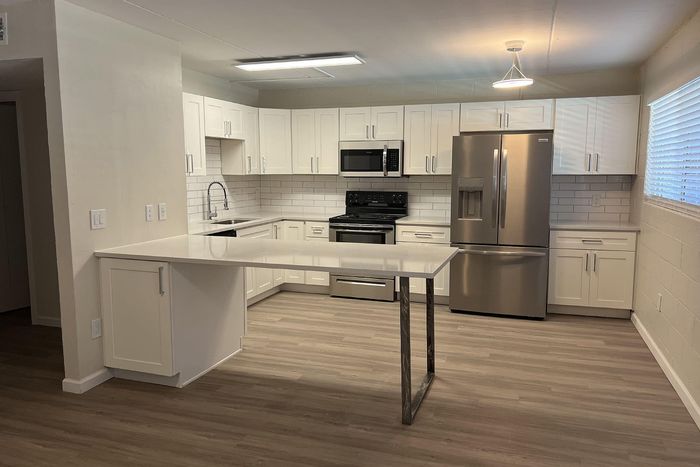 Sleek modern kitchen with white cabinetry, stainless steel appliances, and stylish lighting on wood flooring.