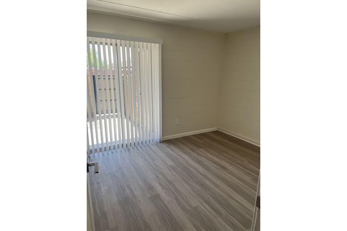 Bright room with sleek wood flooring and tall vertical blinds overlooking a private balcony.