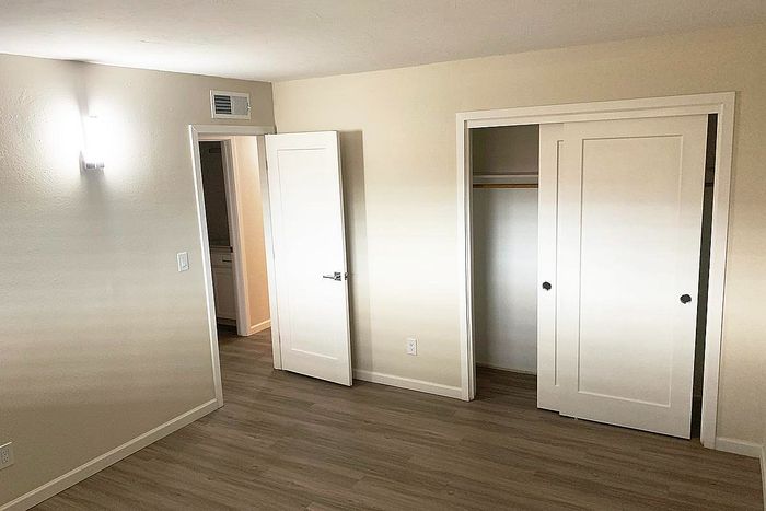Bright and inviting bedroom with sleek hardwood floors, modern closet space, and ample natural light.