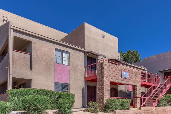 Charming apartment exterior with modern architecture, vibrant red accents, and lush greenery under a clear blue sky.