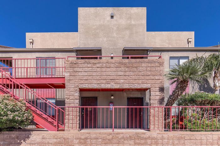 Modern apartment exterior with vibrant red accents and lush greenery, under a clear blue sky.
